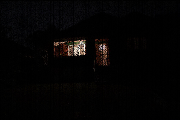 a distorted scene of a brick house with a porch light on during a dark evening